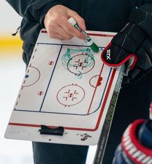 A coach holding a whiteboard and explaining a drill to a player