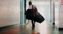 A young kid walking into Hockey Etcetera with a hockey bag over his shoulder and a hockey stick in hand