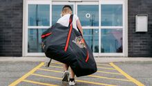 A kid walking into Hockey Etcetera holding a hockey bag and stick