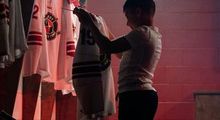 A kid holding up and starting at a Hockey Etcetera hockey jersey in the dressing room