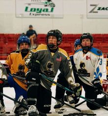 Young kids in various colourful hockey jerseys kneeling and listening to the coach on the ice at Hockey Etcetera's Mentorship camp.