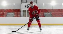 A hockey player with their stick on the ice in a full red Hockey Etcetera uniform