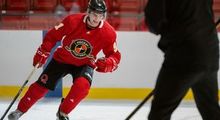 A hockey player stopping on the blue line while a coach watches