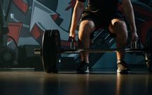 A man bending down to deadlift in the Junxion Performance gym with dark lighting