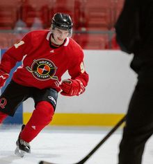 A hockey player stopping on the blue line while a coach watches