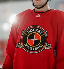 A close-up of a hockey player from the chin to the waist wearing a red Hockey Etcetera practice jersey