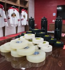 Tape and water bottles sitting on the dressing room table at Hockey Etcetera with jerseys hanging in the stalls in the background