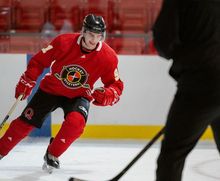 A hockey player stopping on the blue line while a coach watches
