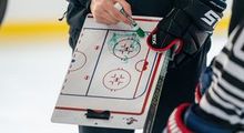 A coach holding a whiteboard and explaining a drill to a player