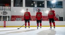 Three hockey players lined up on the ice in full red Hockey Etcetera uniforms