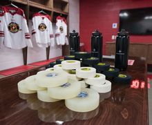 Tape and water bottles sitting on the dressing room table at Hockey Etcetera with jerseys hanging in the stalls in the background