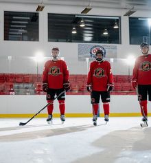 Three hockey players lined up on the ice in full red Hockey Etcetera uniforms