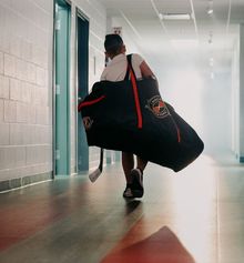 A young kid walking into Hockey Etcetera with a hockey bag over his shoulder and a hockey stick in hand
