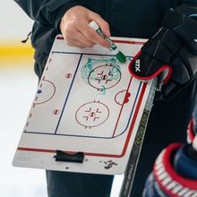 A hockey player stopping on the blue line while a coach watches