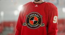 A close-up of a hockey player from the chin to the waist wearing a red Hockey Etcetera practice jersey