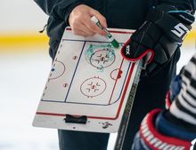 A coach holding a whiteboard and explaining a drill to a player