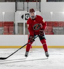 A hockey player with their stick on the ice in a full red Hockey Etcetera uniform